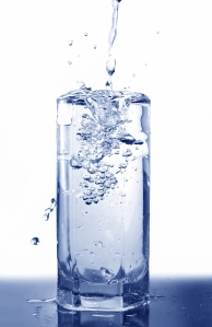 Big long drop of cold water poured into full glass (isolated on white background)